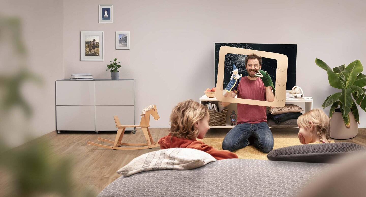 Ein Vater spielt Puppentheater für seine Kinder vor einem kaputten Fernseher